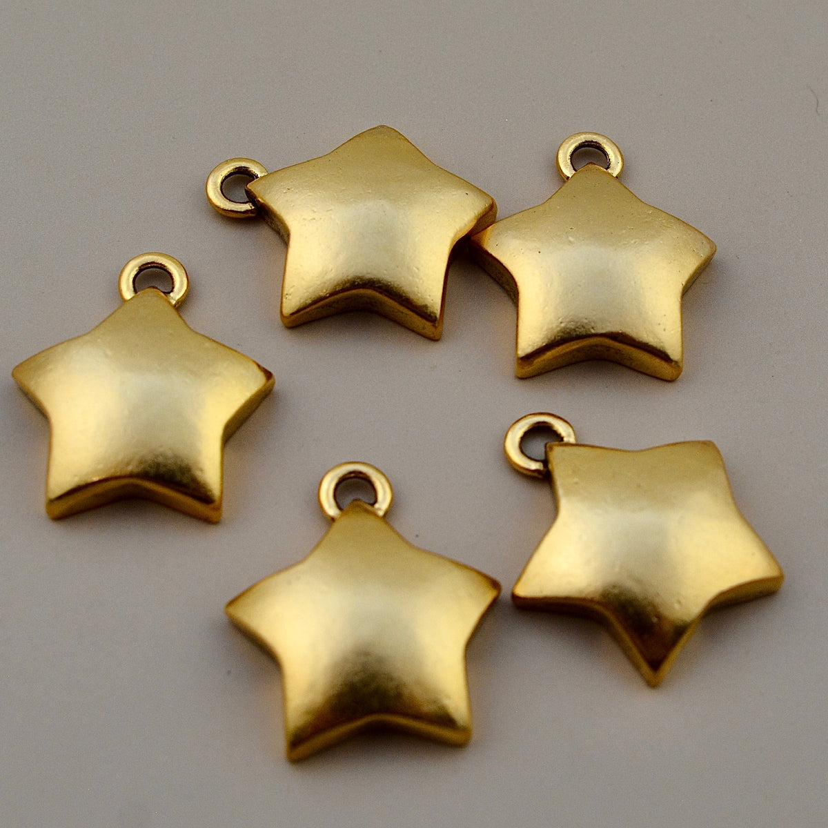 Close-up view of smooth gold star pendants with loop attachments on a gray background