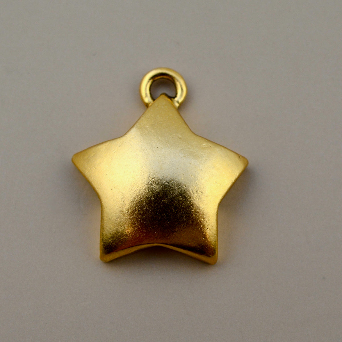 Front view of medium smooth gold star pendant charm showcasing its domed surface and top loop on a gray background