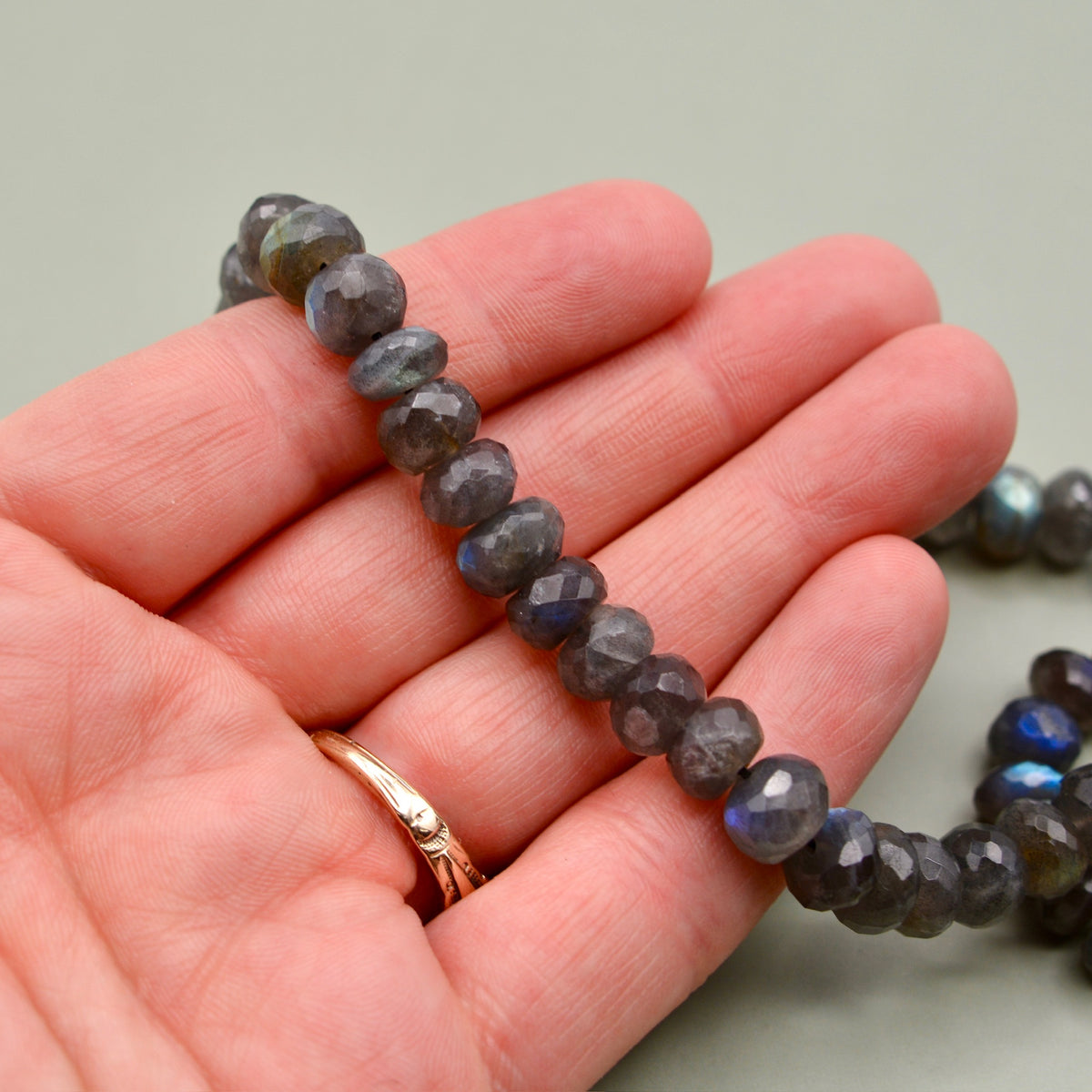 Close-up of black iridescent labradorite 7 to 8mm faceted rondelle bead strand showcasing faceted beads in hand