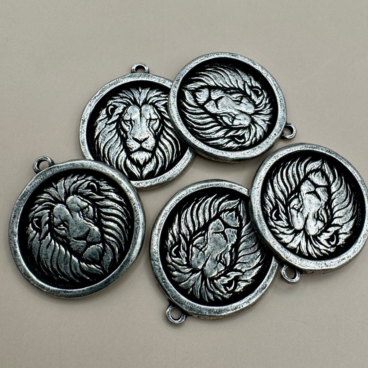 Close-up of antiqued pewter circle lion pendants showcasing raised lion designs and looped findings on a neutral background