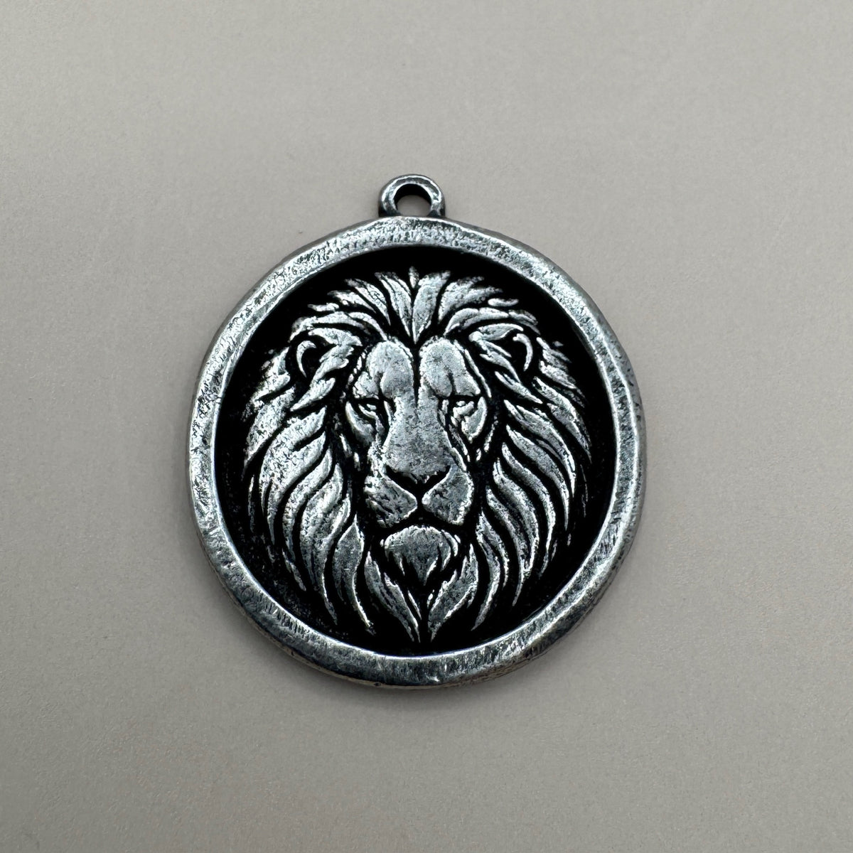 Front view of a lion pendant showcasing a raised lion face in an antiqued pewter finish with a neutral background
